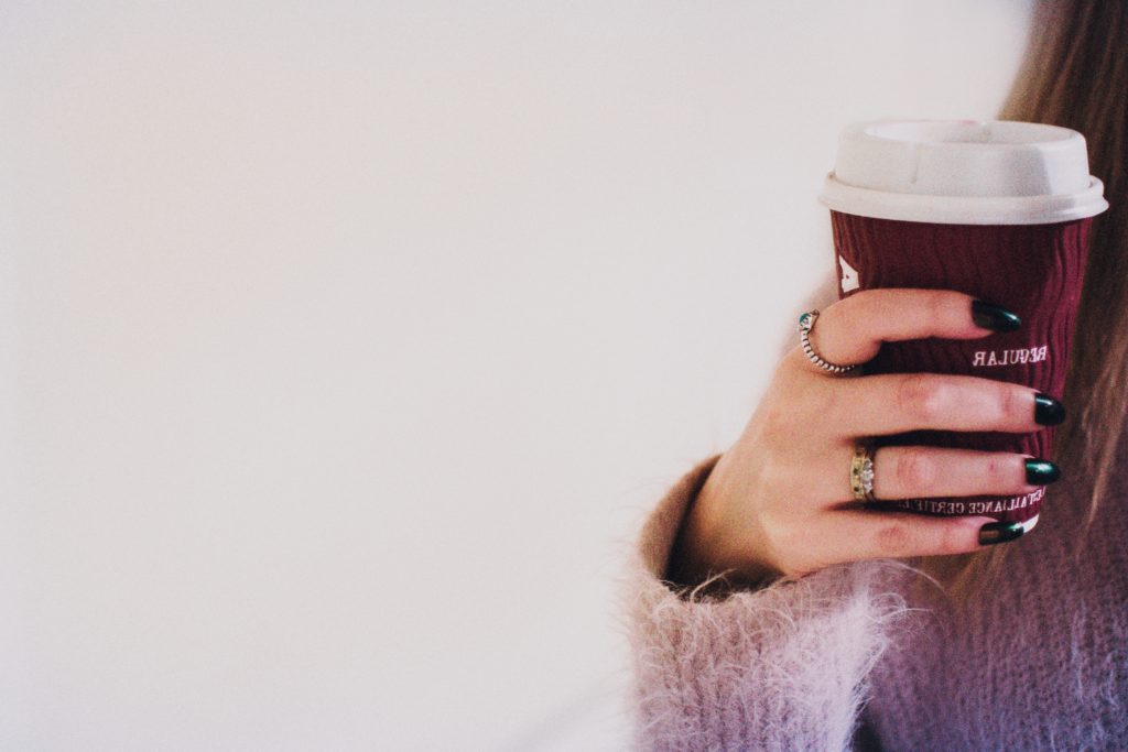 person with black manicured nails holding brown cup with 850384